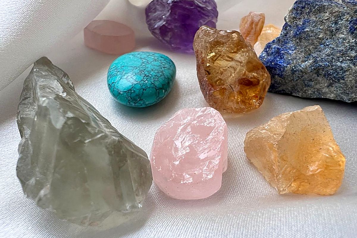 Raw semi precious gemstones on white silk — rose quartz, amethyst, turquoise, citrine and lapis lazuli.